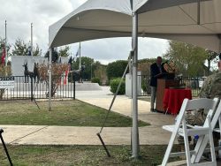 Keynote speaker, John Burnam, stands in front of the Military Working Dog Teams National Monument to provide his address.